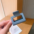 Detailed close-up of a square matte grey-blue hair claw clip held in hand - Blue