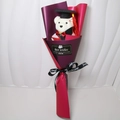 Detail view of graduation plush bear in black cap and gown within purple gift wrap - Burgundy