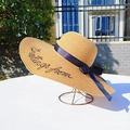 Beige wide brim straw sun hat with navy ribbon and Greetings From embroidery on white table - M (56-58cm) / Khaki (Greetings From Embroidery)