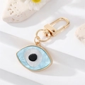 Golden Evil Eye keychain with blue marble texture on white stone background - Evil Eye Patch
