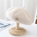 Detail view of cream wool beret with gold double-ring emblem on a wooden stand - M (56-58cm) Adjustable / Beige