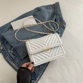 White V-quilted faux leather shoulder bag with golden chain strap and lock on denim - White