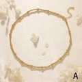 Détail du collier à perles dorées avec fermoir mousqueton et chaîne de réglage sur fond de pétales - Style perle dorée