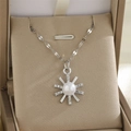 Détail du pendentif soleil argenté avec perle blanche et strass brillants sur l'écrin - Perle Soleil
