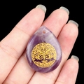 Hand holding a teardrop-shaped purple amethyst pendant with golden Tree of Life carving - Amethyst