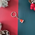 Christmas keychain with red santa hat charm and silver ring on festive pine branch background - Christmas Hat
