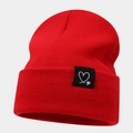 Close-up of the red knitted beanie texture and a black heart label on the folded brim - One Size / Red