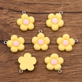 Set of 7 yellow resin flower charms with pink centers and metal loops on wood background - Yellow