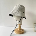 Dettaglio di cappello da sole beige in nylon con cordino antivento e piccola etichetta - Beige