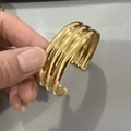 Detail view of a wide gold-plated wavy cuff bracelet worn on hand with glossy finish - Gold Wave Pattern