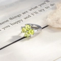 Silver clover earring with light green heart stones against a blurred book page background - Fruit Green Clover Ear Hoop (A704-2#)