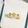 Top view of a gold flower ring with yellow and green gemstones in a velvet box - Yellow Oval Gemstone with Green Square Side Stones Style (金色17)