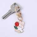 Detail of a white enamel rabbit keychain holding a red rose with golden metal finish - Flower Rabbit