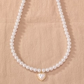 Detail of white pearl necklace featuring a gold-edged heart pendant on beige linen fabric - White