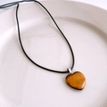 Détail d'un pendentif cœur en œil de tigre avec cordon noir sur une assiette en céramique - Style Oeil de Tigre