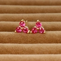 Macro view of gold clover stud earrings with three red round-cut gemstones in prong setting - Gold/Rose Red Zirconia