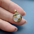 Dettaglio macro di un ciondolo tondo dorato con due intarsi in madreperla a cuore - Cuore