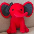 Adorable red plush elephant toy with black bow tie sitting on soft fabric background - Red