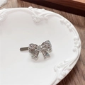 Close-up of a silver Y2K bow hair clip with sparkling rhinestones on a ceramic tray - Bow / White