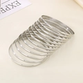 Close-up of polished 3.6mm silver stainless steel stackable bangles on a textured surface - Inner Diameter 68mm / Set of 12 / Steel