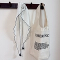Detail of a beige canvas tote bag with letter print and a white scarf with grey trim - White