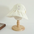Detail of cream sun hat with purple floral patterns and wavy brim on wood stand - 52cm (3-6 Years) / Light Yellow