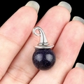 Witch hat pendant featuring a blue glittery stone held on a finger for size - Blue Sand Stone (Synthetic)