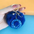 Close-up of blue pom pom keychain with gold ring, resin letter pendant, and soft tassel - Letter O