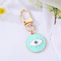 Hellblauer Evil Eye Schlüsselanhänger mit goldenem Karabinerverschluss auf weißem Stoff - Hellgrünes Wimpern-Emaille-Auge