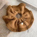 Detailed texture of brown knit scrunchie with a delicate bow and gold metal tag - Brown