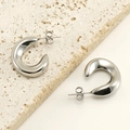 Primer plano de pendientes de aro en C de acero inoxidable pulido sobre piedra beige - Color Acero