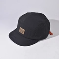 A detailed macro view of the black short-brim five-panel cap showing the fabric and logo - Adjustable / Black