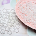 Macro view of white heart-shaped faux pearl beads for DIY crafts on a pink tray - White