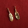 Pair of gold-plated S925 silver feather charms on textured red fabric background - Feather (G)CD316