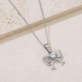 Macro shot of a silver bow necklace with a clear zircon stone on a white stone background - Matte Bow Knot with Zirconia (NKS-002_04A)