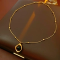 Primer plano de un collar con colgante de ojo de tigre dorado sobre cuero marrón - Collar-Dorado-Marrón