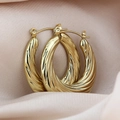 Golden titanium steel twisted hoop earrings on soft pink satin fabric background - Shell Texture / Gold