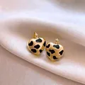 Gros plan de boucles d'oreilles cœur dorées avec motif vache sur fond en soie - Style Imprimé Vache en Forme de Coeur Or