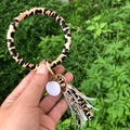 Leopard print PU leather bracelet keychain with white tassel held against green plants - Camo Brown Leopard