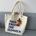 Detail einer beigen Canvas-Tasche mit orangefarbenem Plüsch-Anhänger und blauem Text - Mit Orangenanhänger / Gebrochenes Weiß