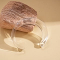 Macro shot of a transparent acrylic open bangle on a natural stone base with soft warm lighting - Clear