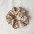Elegant champagne gold satin scrunchie hair tie with smooth silk texture on fabric - Champagne