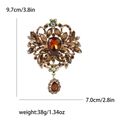 Broche vintage dorée avec grand cristal ambré et pendentifs en strass sur fond blanc - Marron