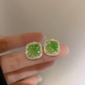 Detail of square green crystal earrings with halo zircons held between fingers - 2# Silver Earring Post - Green Square Inlaid with White Zirconia Style (HE9329)