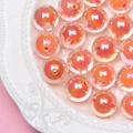 Close-up of DIY iridescent orange-pink beads with a hole on a white embossed plate - Orange