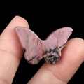 Polished pink rhodonite crystal butterfly carving with natural black veins held by hand - Rhodonite