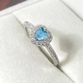 Close-up of heart-shaped blue gemstone ring with zircon inlay in a white jewelry box - Platinum + Aquamarine