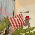 Dettaglio della borsa da trucco a righe rosa e marroni in tela con etichetta bianca sobria - Righe Rosa e Marroni