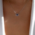 Close-up of Evil Eye pendant with blue stone and pavé accents on white blazer - Silver O-chain Blue Stone Eye Pendant