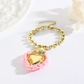 Makroaufnahme von Goldperlenarmband mit rosa umrandetem Herzanhänger und Karabinerverschluss - Rosenrosa